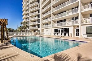 A swimming pool with lounge chairs and a multi-story building with balconies.