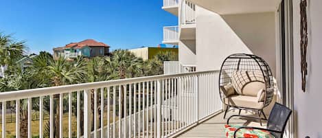 A balcony with a white railing, a hanging chair, and two chairs with floral upholstery.