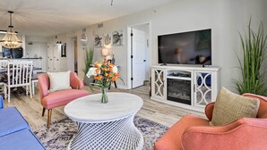 A living room with a round coffee table, a television, and a dining area with a white cabinet and a chandelier.