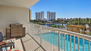 A balcony with wicker furniture, a pool, and a view of tall buildings.