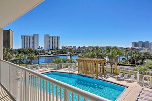 A pool area with lounge chairs and a gazebo, surrounded by palm trees and a view of high-rise buildings. - Snowbird's Retreat: Walkable Destin Condo w/ View! (Destin)