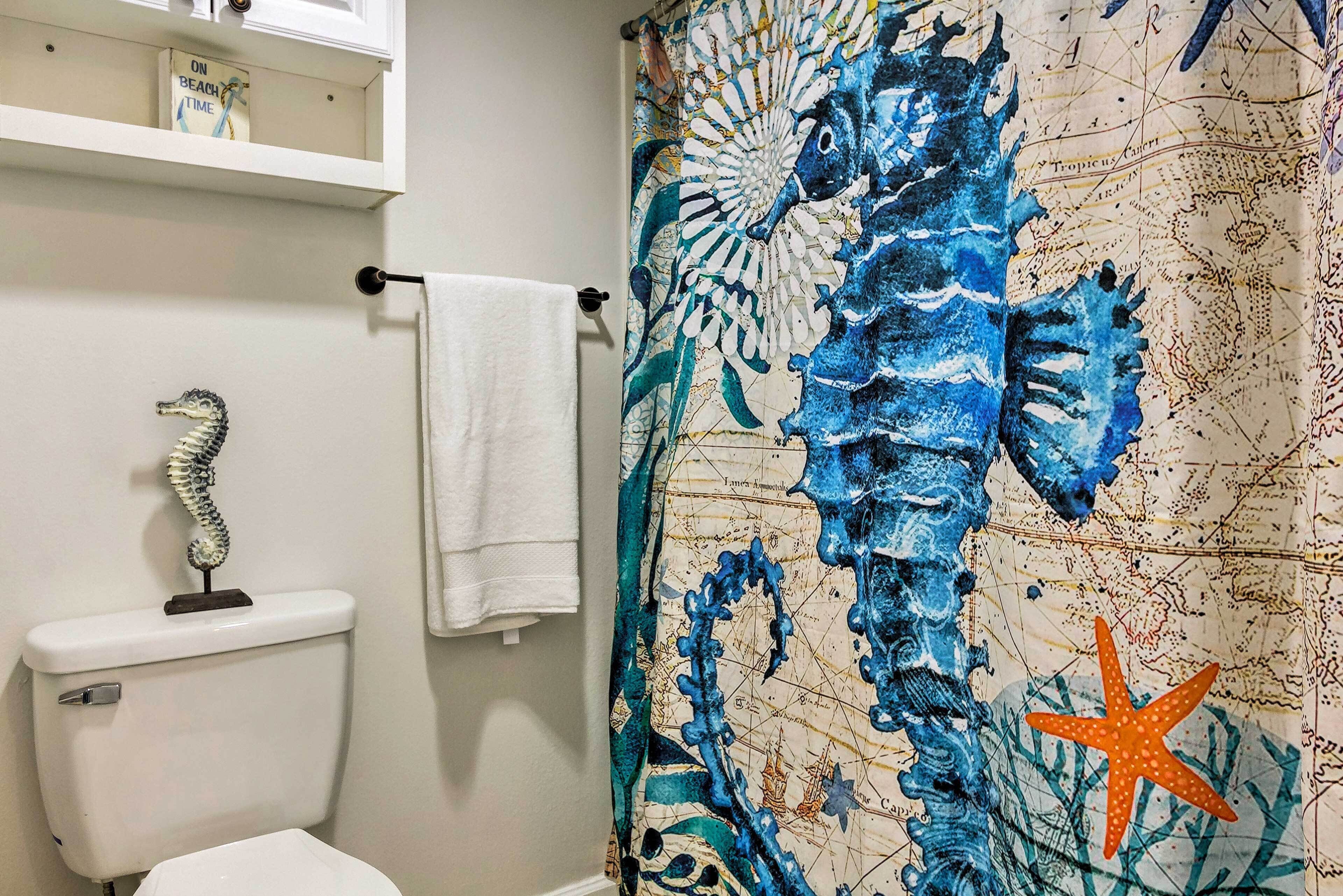 Un baño con un adorno de caballito de mar en el inodoro, una toalla blanca colgada en un perchero y una cortina de ducha con diseño de mapa náutico.
