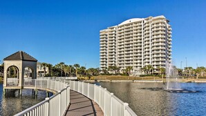 A waterfront promenade with a white bridge, a fountain, and a tall hotel building.