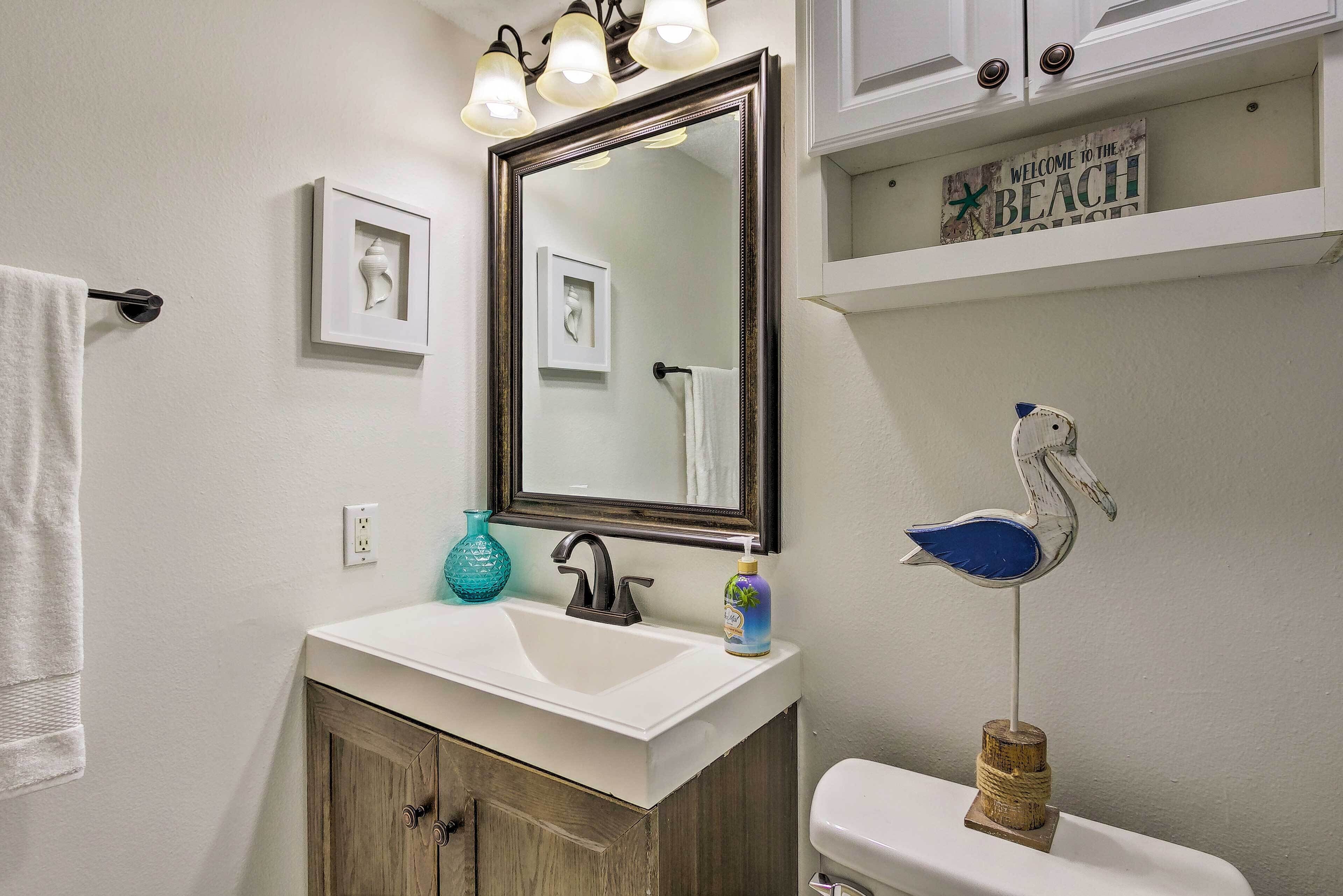 A bathroom with a white sink, a large mirror, and a toilet. There are decorative items on the wall, including a swan-shaped soap holder and a welcome sign.