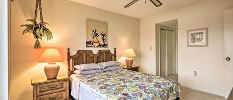 A bedroom with a bed, two bedside tables with lamps, a ceiling fan, a wall-mounted plant, and a door.