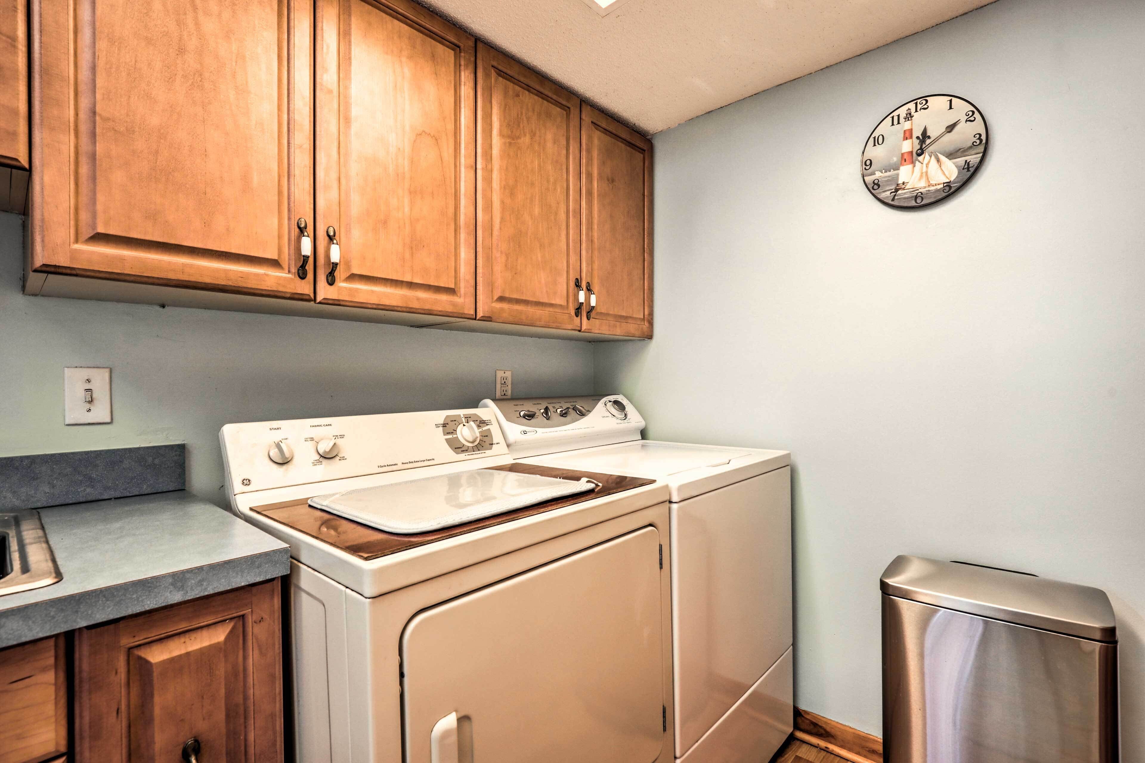 A kitchen with wooden cabinets, a stove, a washing machine, and a trash bin.