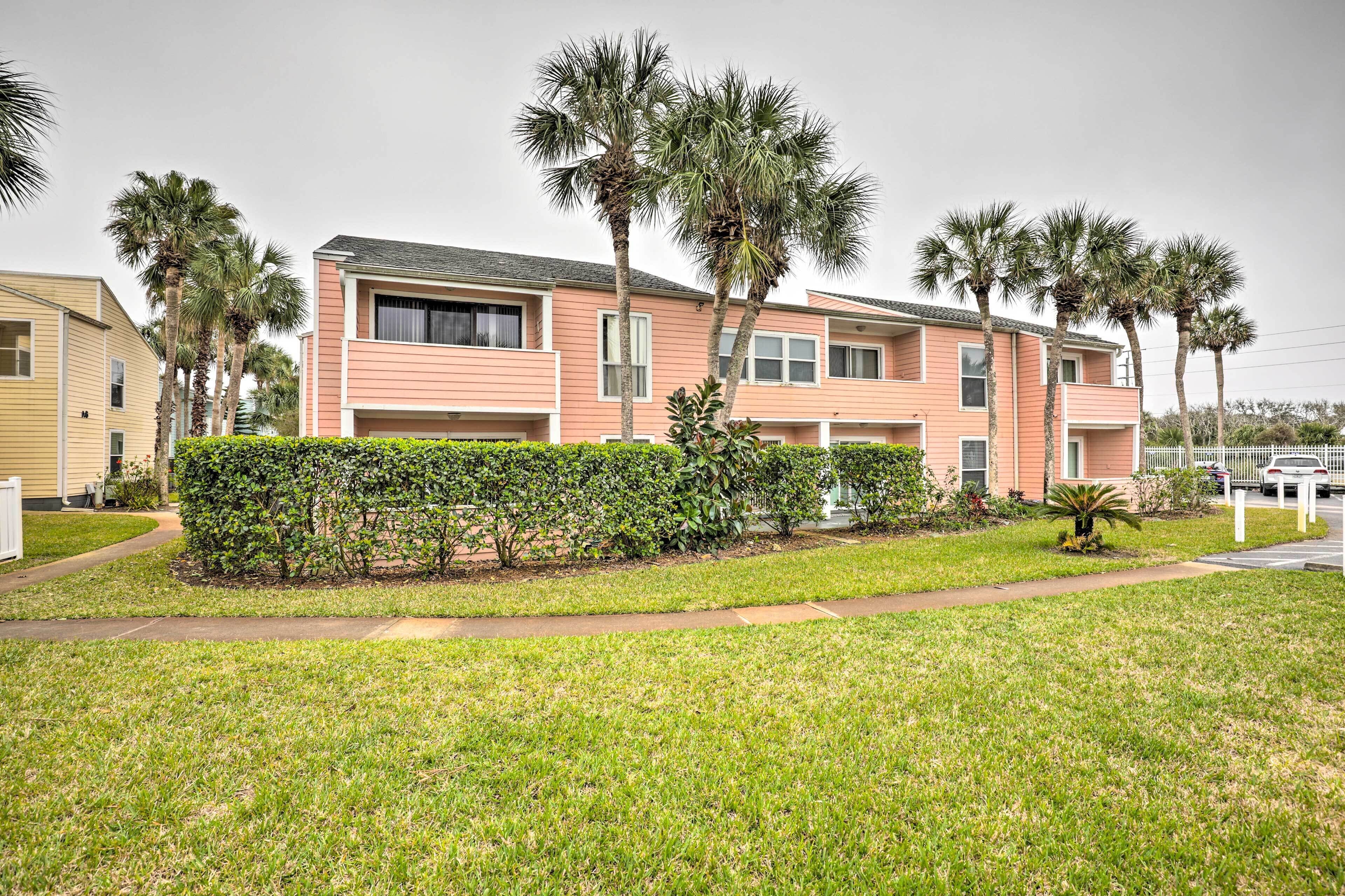 A row of pink apartment buildings with a grassy lawn and palm trees.
