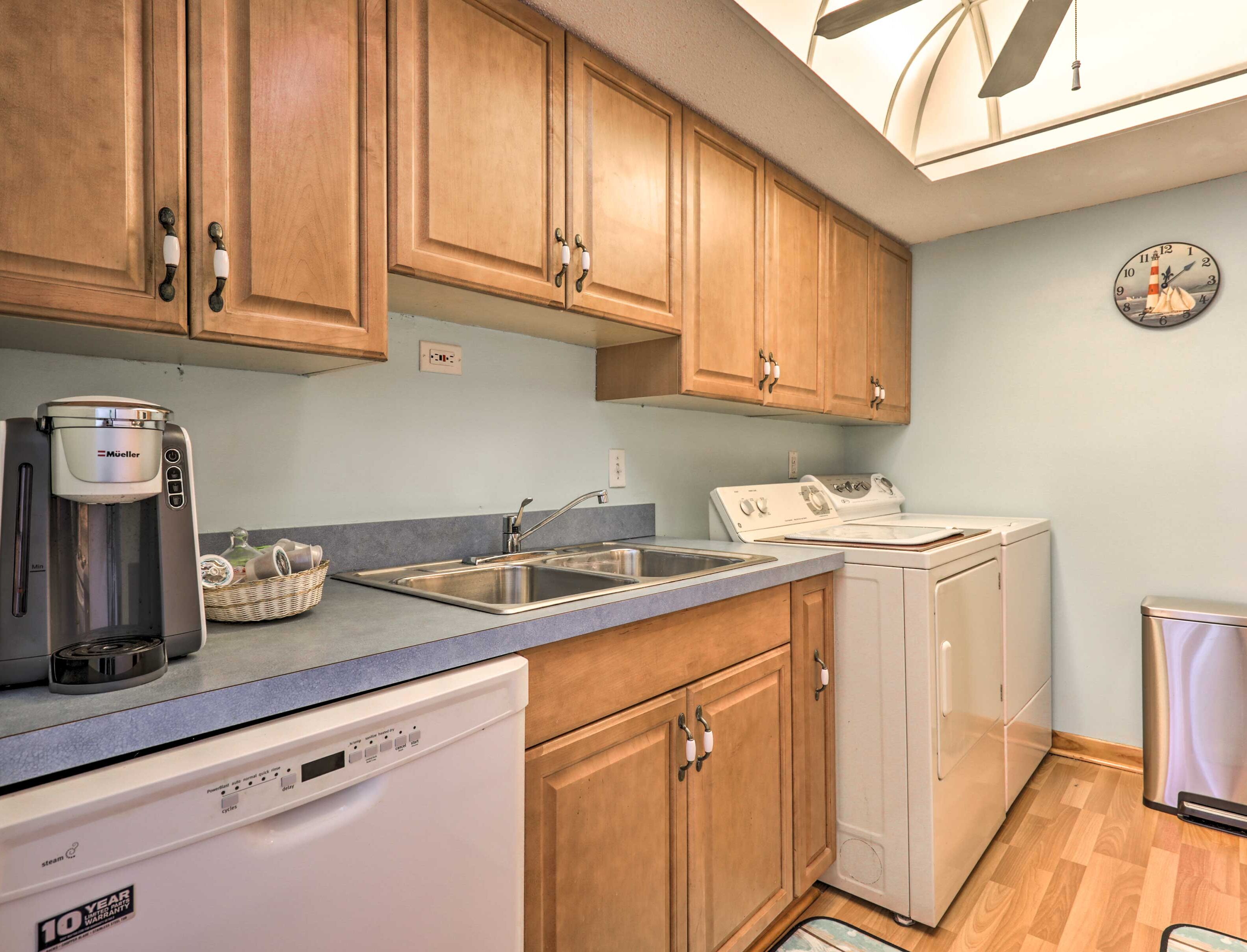A kitchen with wooden cabinets, a coffee maker, a dishwasher, a stove, and a clock on the wall.