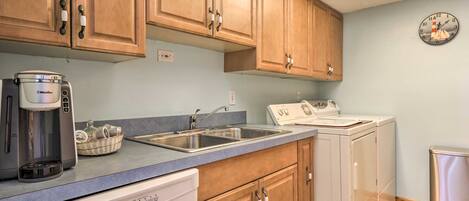 A kitchen with wooden cabinets, a coffee maker, a dishwasher, a stove, and a clock on the wall.