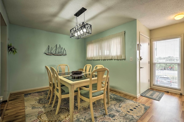 Un comedor con una mesa y sillas, una lámpara colgante, una ventana con cortinas y una puerta que da al exterior.