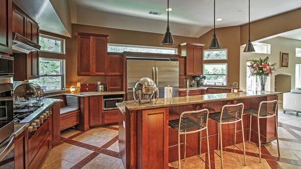 A kitchen with wooden cabinets, a stainless steel refrigerator, a built-in island with bar stools, and pendant lighting.