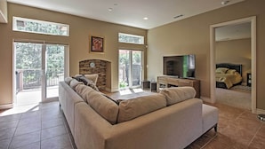 A spacious living room with a large beige sofa, a fireplace, and a television. There are large windows and a balcony visible.