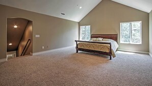 A bedroom with a sloped ceiling, a bed, two windows, and a carpeted floor.