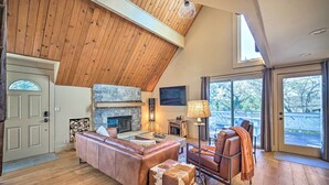 A spacious living room with a stone fireplace, leather furniture, and a high wooden ceiling.