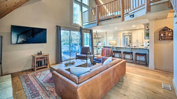 A spacious living area with a large leather sofa, a wooden coffee table, and a patterned rug. A television is mounted on the wall, and there is a staircase leading to an upper level.