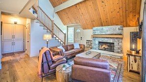 A spacious living room with a high wooden ceiling, a stone fireplace, leather sofas, and a staircase leading to another level.