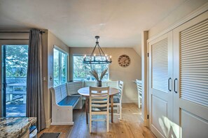 A dining area with a round table, chairs, a chandelier, and a view through large windows. - Lake Arrowhead Cabin w/ Balcony, Near Trails (Lake Arrowhead)