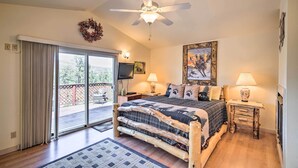 A bedroom with a bed, two bedside lamps, a ceiling fan, a fireplace, and a view of the outdoors.