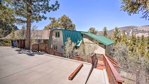 A residential property with a green-roofed house, a covered patio, and a view of the surrounding hills.