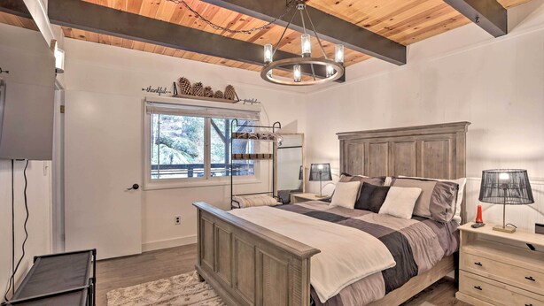 A bedroom with a wooden bed, bedside tables, a nightstand, a chandelier, a window with a view, and a door with a shelf above it.