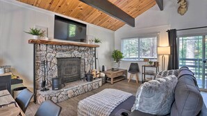 A cozy living room with a stone fireplace, wooden ceiling beams, a comfortable sofa, and a TV mounted above the fireplace.