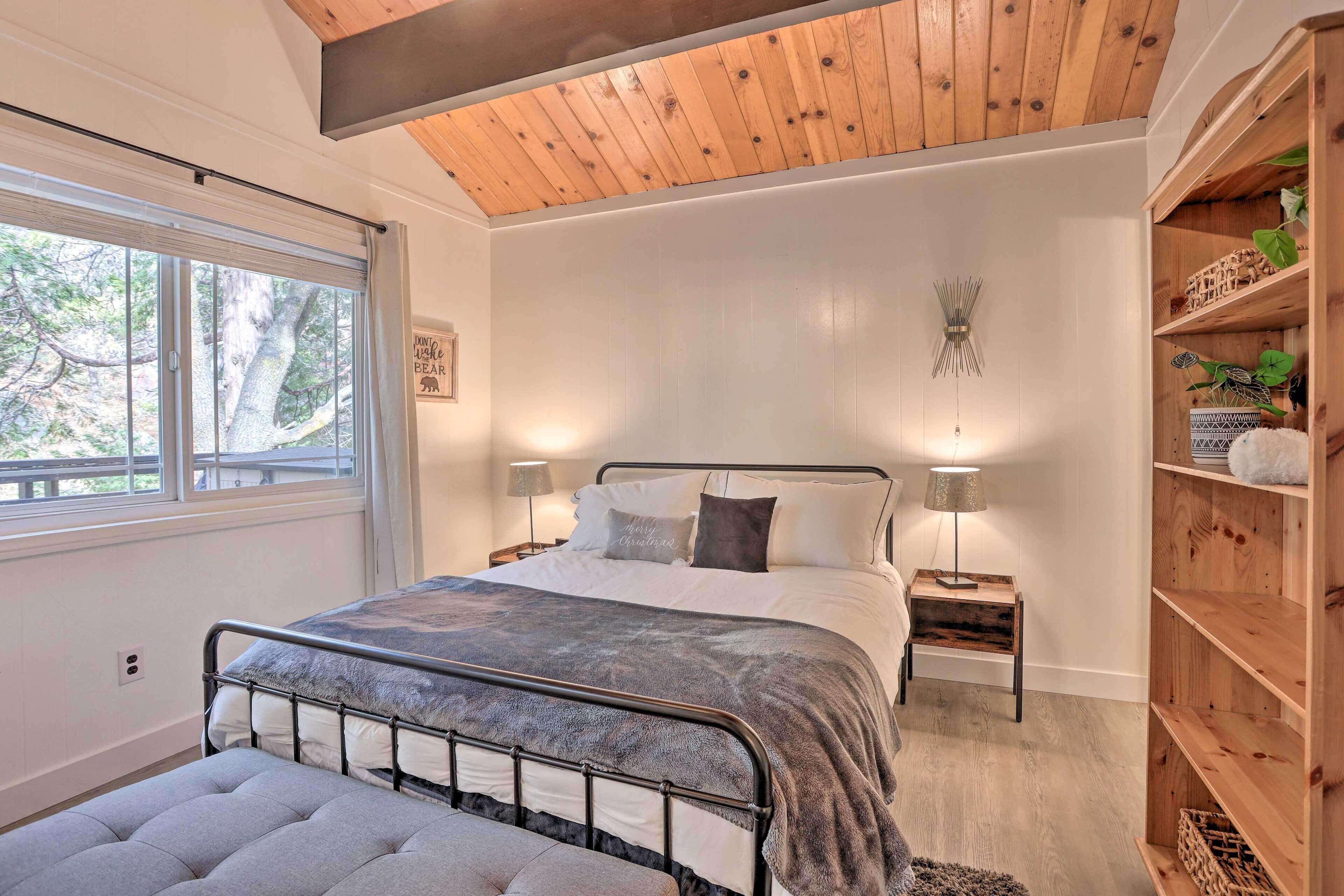 A bedroom with a bed, bedside tables, a bench, a wooden shelf, and a window with blinds.