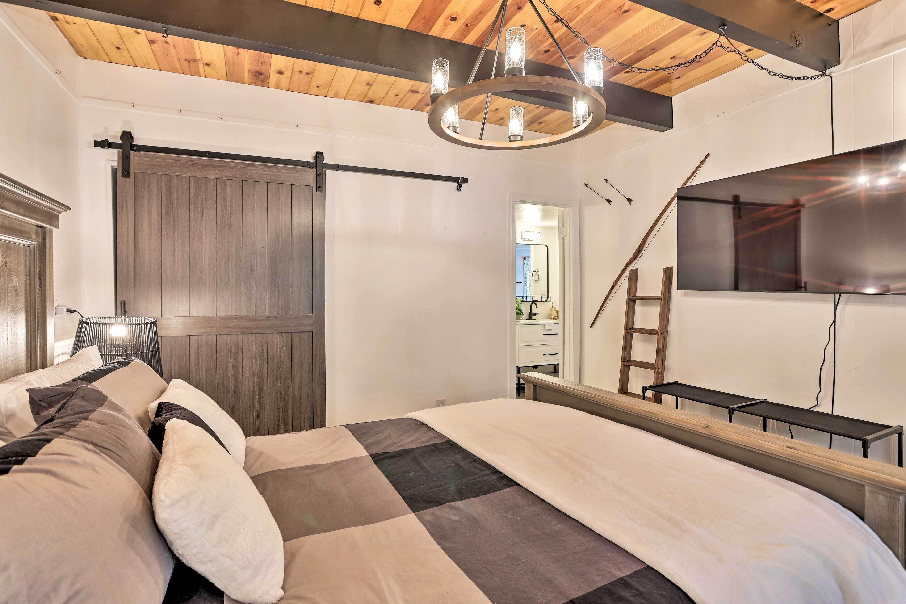 A bedroom with a large bed, a wooden ceiling, a sliding barn door, a TV mounted on the wall, and a ladder.