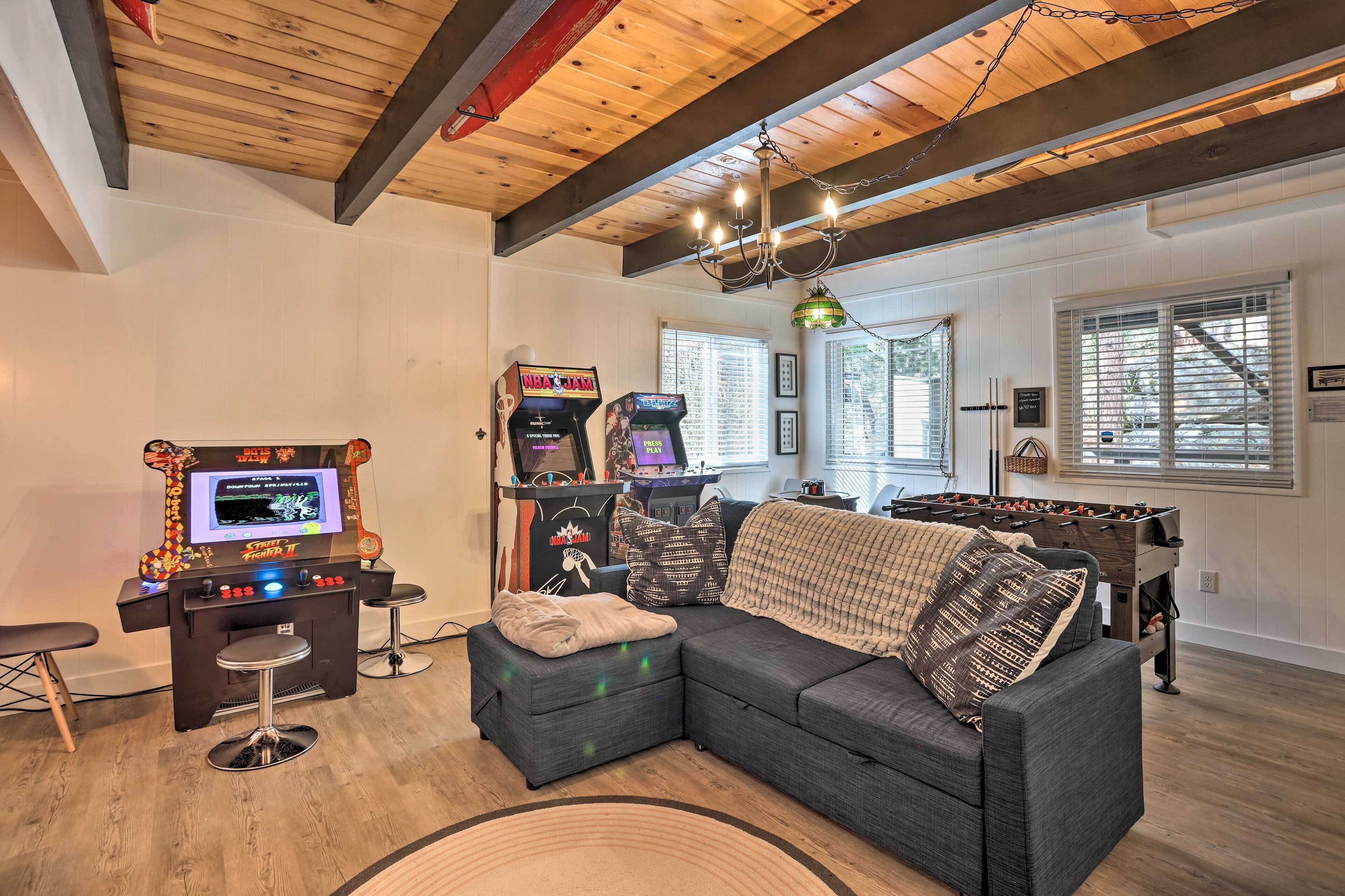 A cozy living room with a sectional sofa, a foosball table, and arcade games.