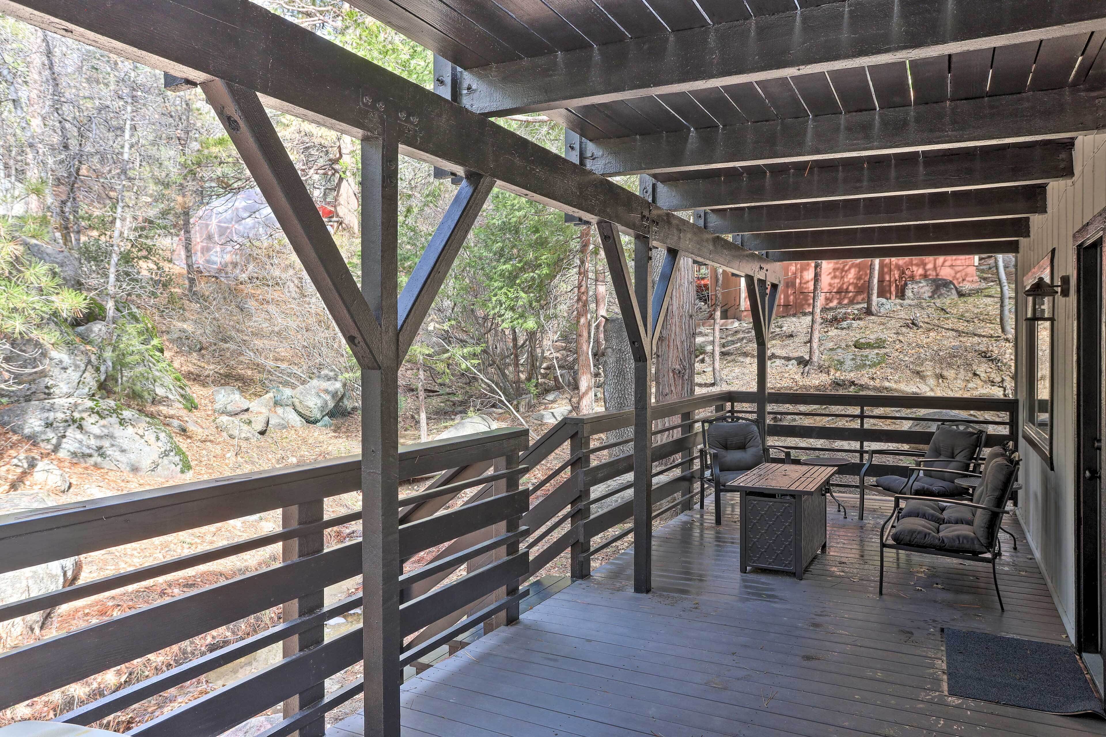A wooden deck with a railing, outdoor seating, and a view of a forested area.