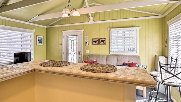 Una cocina con una isla central, un área de comedor con sillas, un sofá y una ventana con persianas.