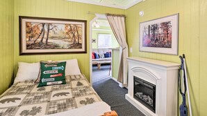 Una habitación con cama, chimenea y dos cuadros. Hay un cojín verde con flechas direccionales y palabras como 'BEARS', 'MOUNTAINS' y 'BEER'.