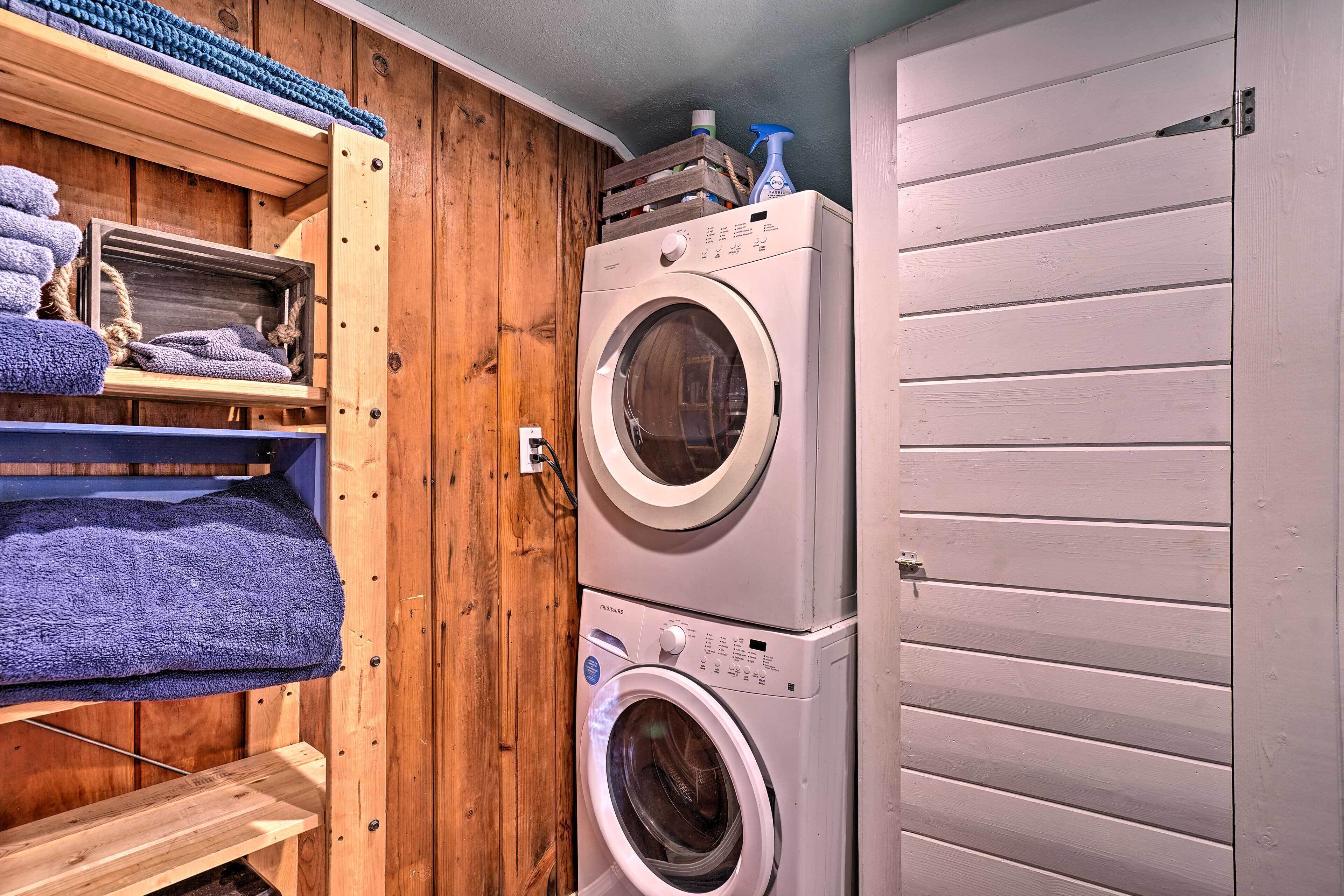 A laundry room with two stacked washing machines, wooden shelves with towels, and a door.