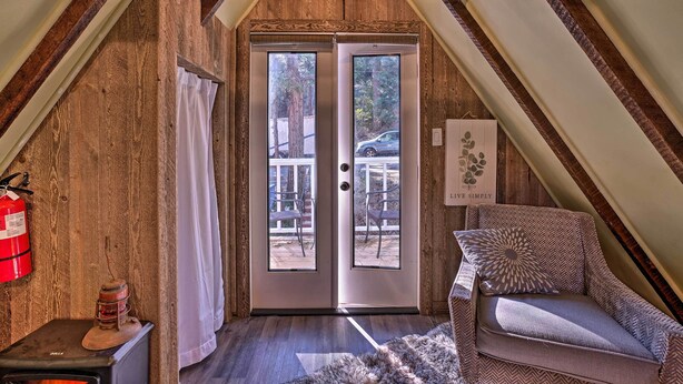 A cozy attic room with a wooden ceiling, a double door leading outside, a fire extinguisher, a heater, and a patterned armchair. - Cozy, Pet-friendly Mtn Cabin: 1 Mi to Lake Gregory (Crestline)