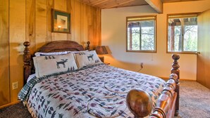 A wooden-paneled bedroom with a bed featuring a deer-themed quilt, a wooden headboard, and two windows. - 5 Mi to Big Bear Mtn Resort: Cozy Cabin w/ Deck (Big Bear City)