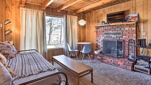Interior acogedor de una cabaña con techo de madera, chimenea, sofá, mesa y televisor.