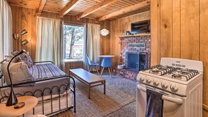 Interior acogedor de una cabaña con una cama, una mesa, un sillón azul, una chimenea y una estufa.