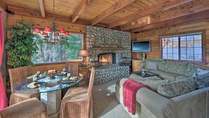 A cozy cabin interior with a stone fireplace, wooden ceiling beams, and a comfortable seating area. - Mountainside Cabin w/ Deck - 16 Miles to Skiing! (Lake Arrowhead)