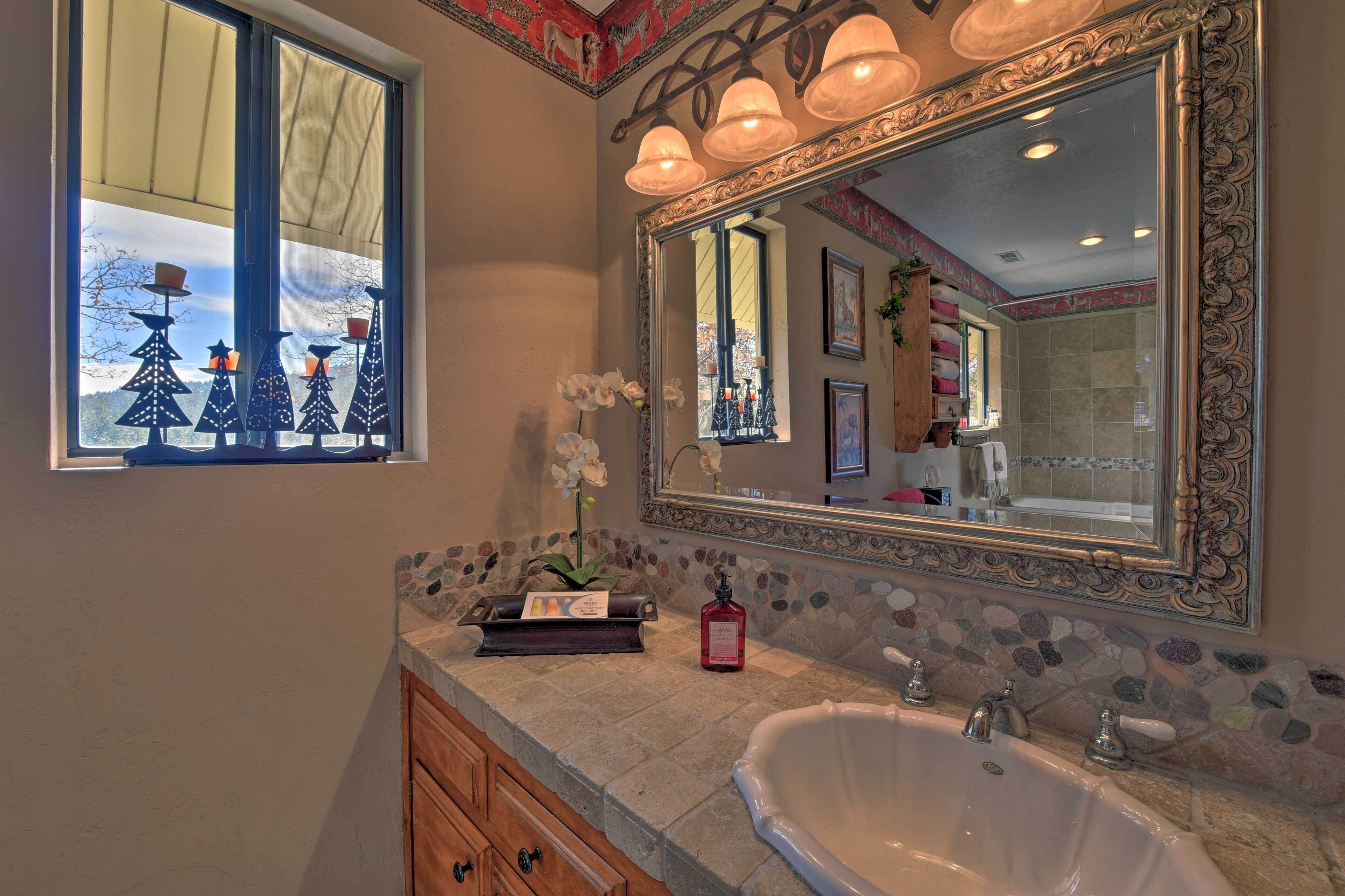 A bathroom with a large mirror, a stone mosaic backsplash, a white bathtub, and a window with decorative Christmas trees.