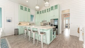 Una cocina con una isla grande, taburetes de bar y un refrigerador de acero inoxidable.