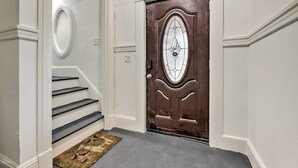 Un couloir avec une porte en bois, un mur blanc et un escalier recouvert de moquette.