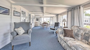 A covered porch with a dining table and chairs, a grey armchair, and a patterned sofa. - Plum Island Retreat ~ 1-block Walk to Beach! (Newbury)