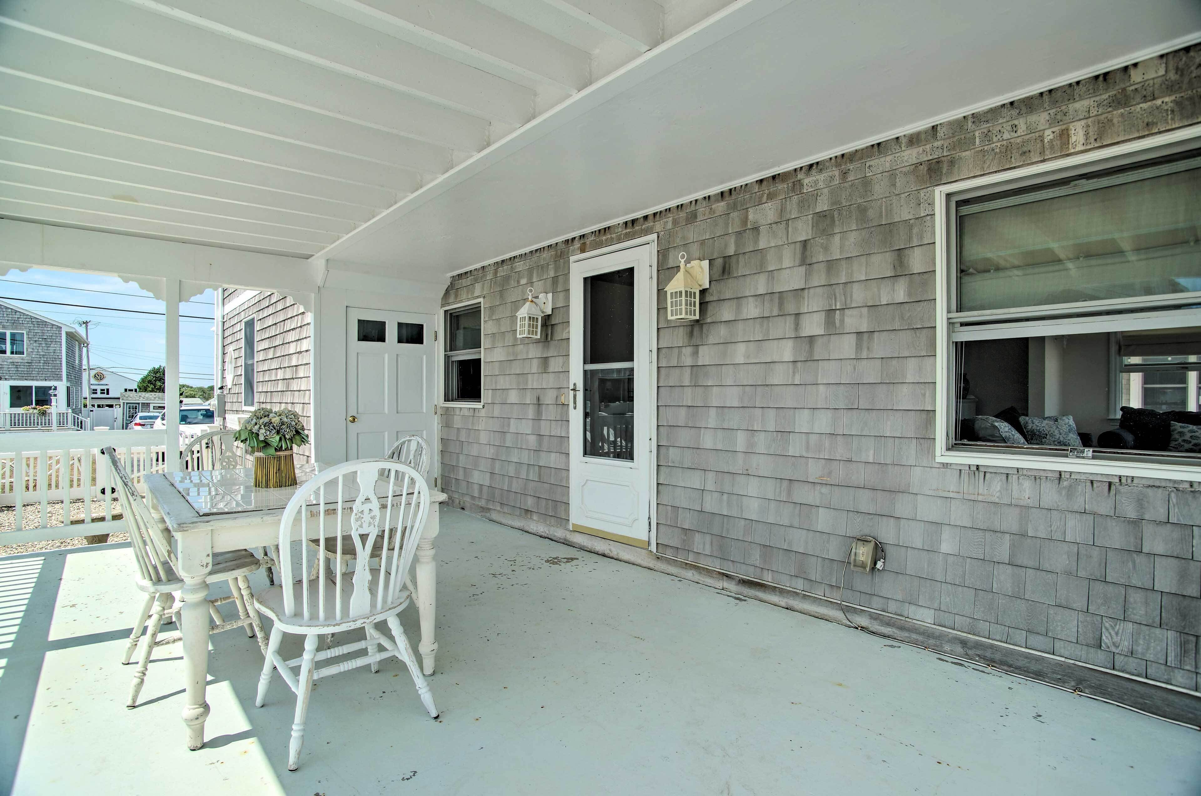 A covered porch with a white table and chairs, a door, and a window with blinds.