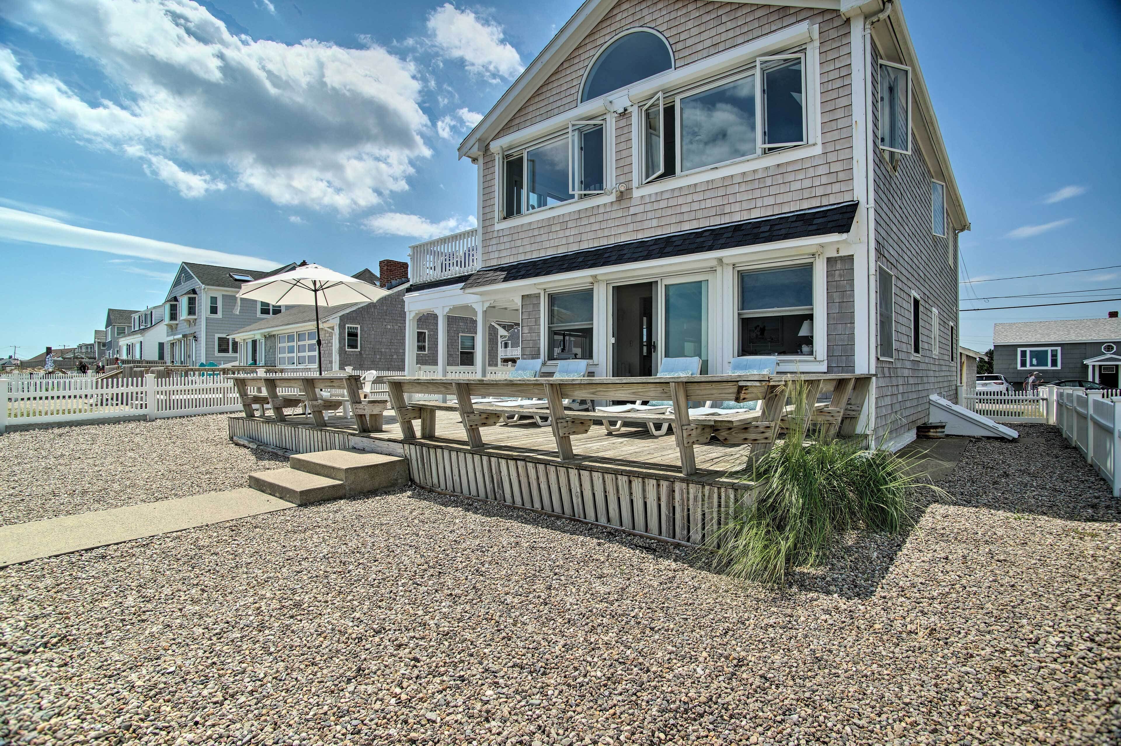 Een huis aan het strand met een overdekt terras en buitenmeubilair.