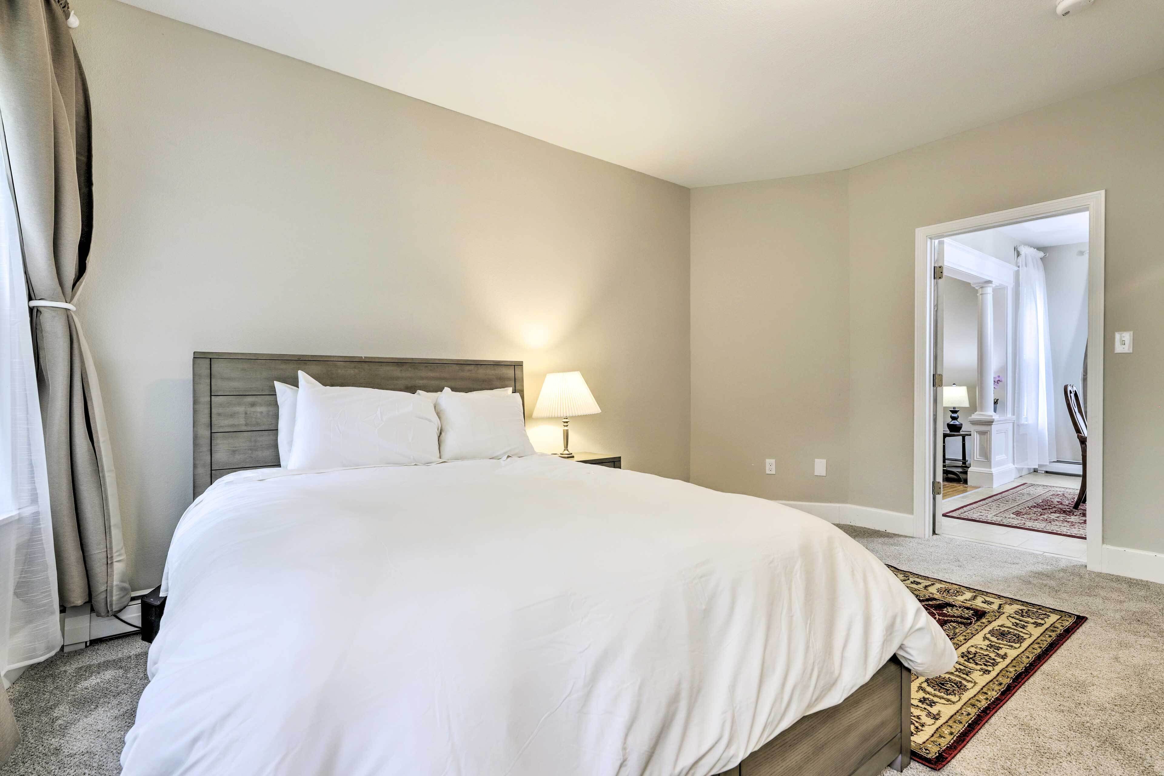 A bedroom with a large bed, a nightstand with a lamp, and a view of a bathroom through an open door.