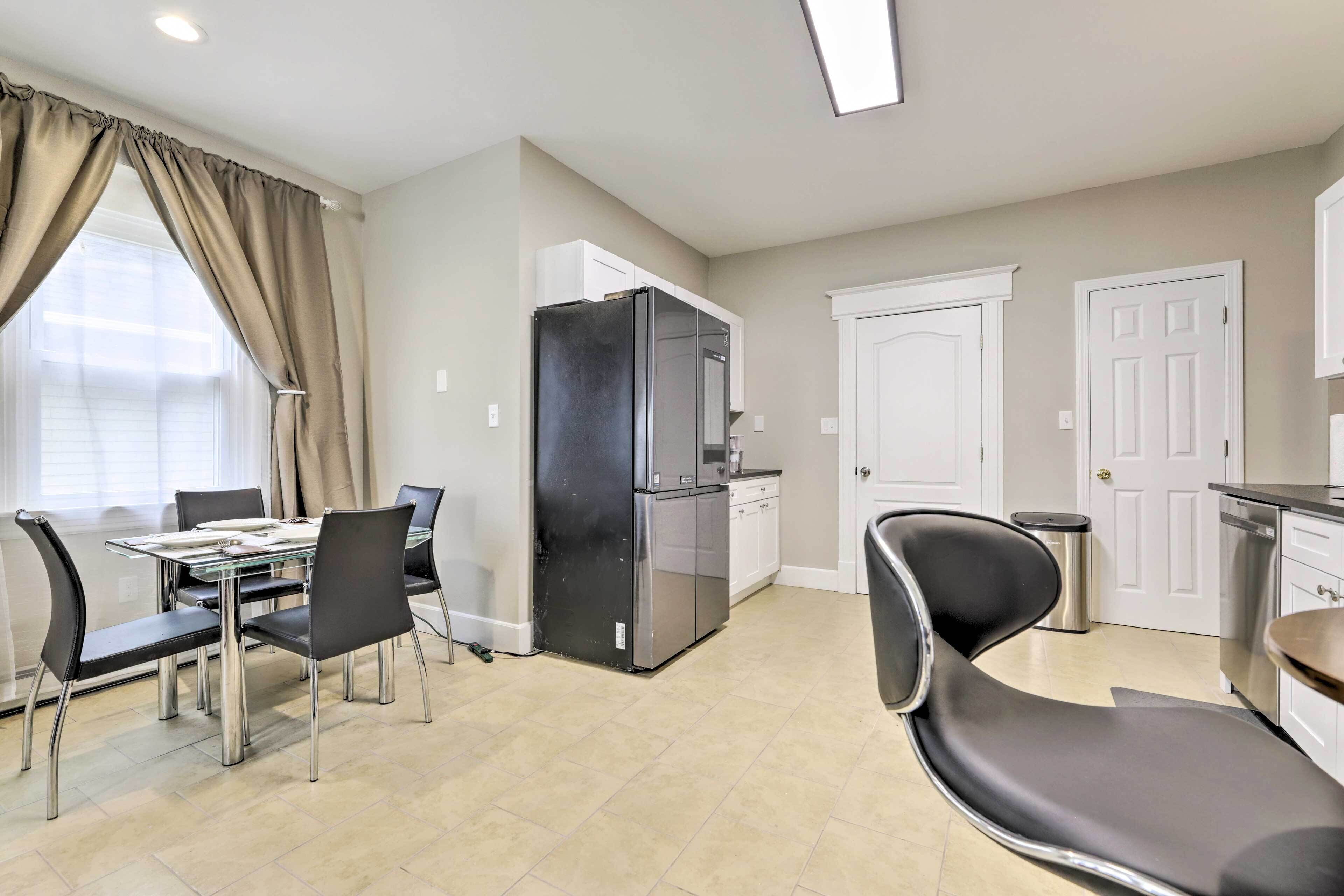 Une cuisine moderne avec un réfrigérateur noir, des armoires blanches et une table à manger avec des chaises.