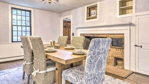A dining room with a wooden table, wicker chairs, a patterned chair, a fireplace, and a chandelier. - Historic Home w/ Modern Updates on < 4 Acres (Royalston)