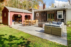 Una cabaña rústica con un patio que incluye una mesa y sillas de madera, un sofá de mimbre y una parrilla.