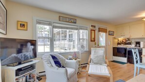 A living room with a TV, white furniture, a fan, and a window with blinds. - Pool & Beach Access: Coastal Condo in Provincetown (Provincetown)