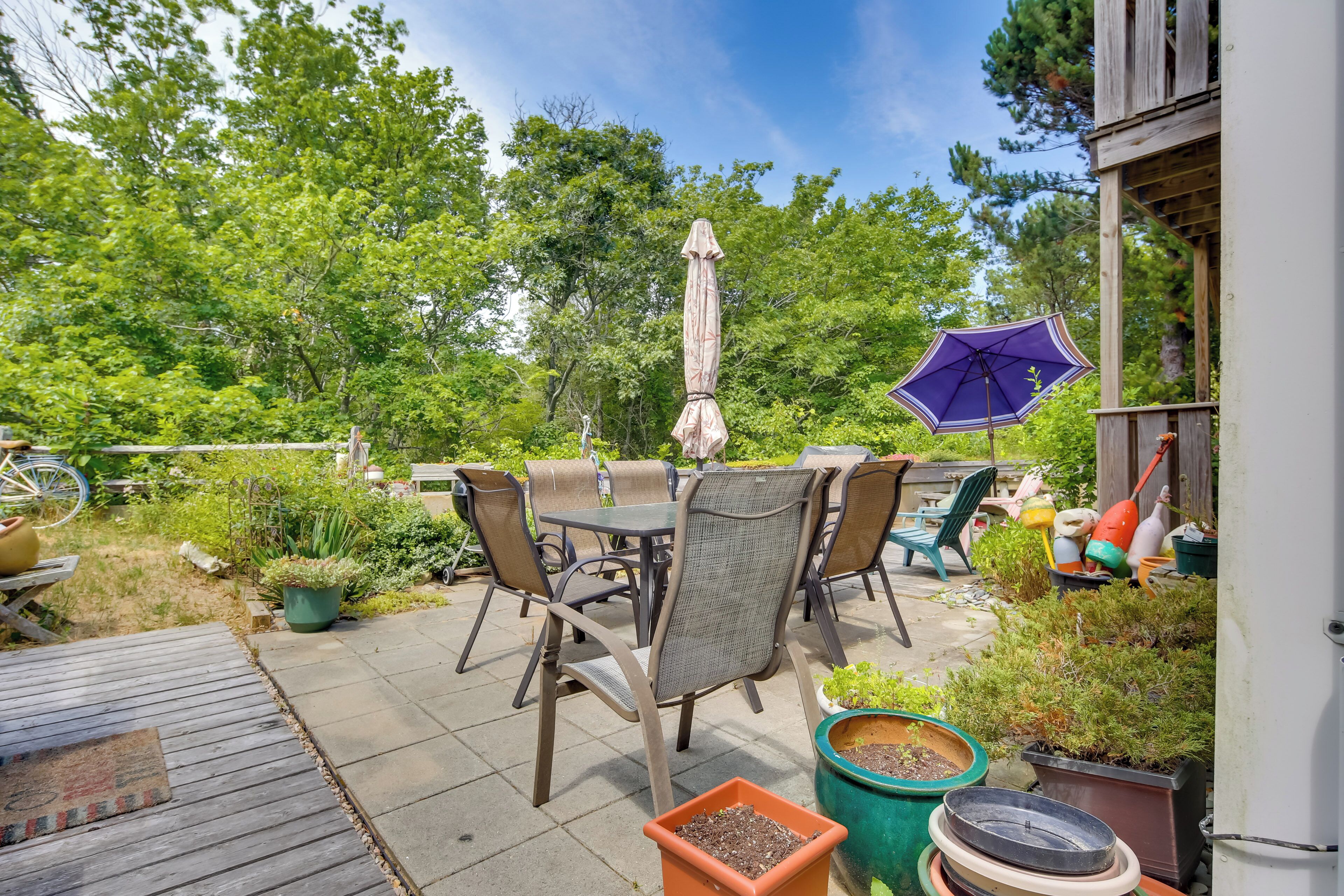 An outdoor patio with a table and chairs, surrounded by potted plants and a wooden deck.