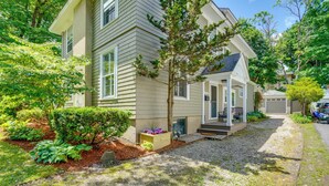 A two-story house with a covered porch, a gravel driveway, and a well-maintained garden with various plants and a wooden planter. - Elegant Pittsfield Home Near Downtown & Skiing! (Pittsfield)